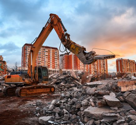 Excavator with crusher and caterpillars on rigging presses pile of reinforced cement parts for material recycling at cloudy sunset