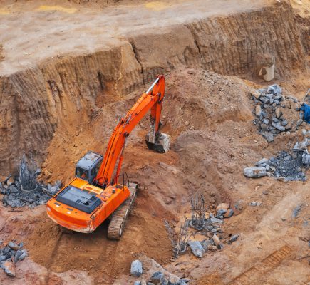 modern orange excavator digs the ground under the foundation pit at a construction site